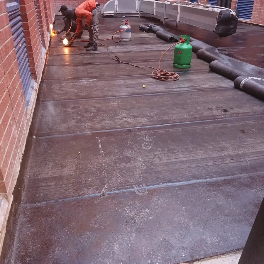Waterproofing team installing torch-on membrane on a flat roof walkway in Cape Town